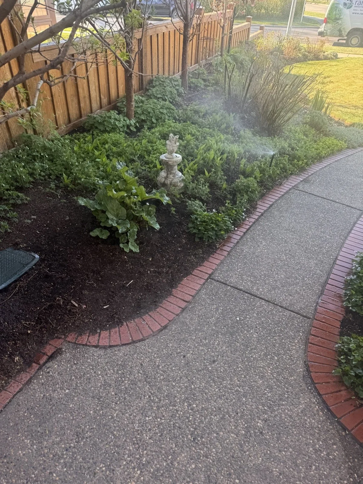 A micro spray watering perennials along a brick-edged path