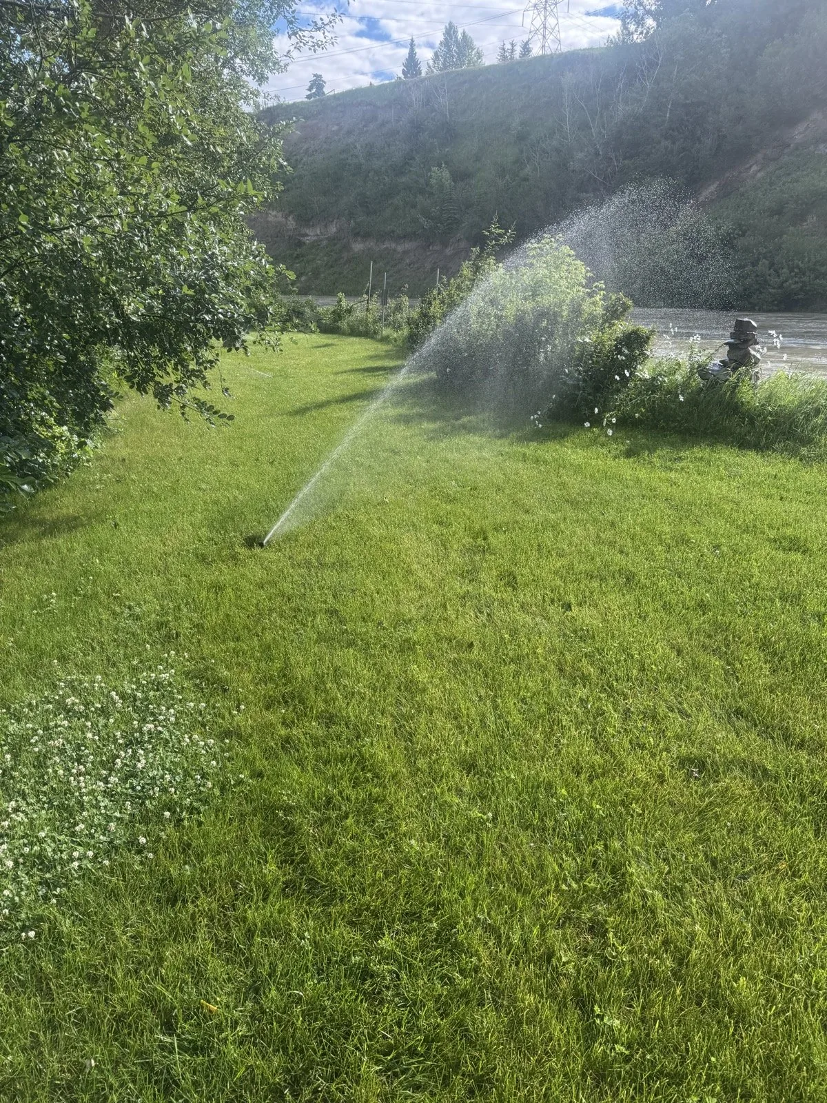 Rotor heads throwing long arcs across an open lawn below a treed slope